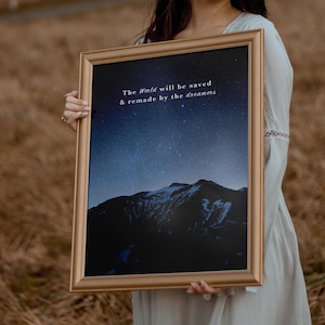 Peut inclure: Un cadre doré contenant une impression d'un ciel étoilé au-dessus d'une montagne. Le texte "The World will be saved & remade by the dreamers" est inscrit sur l'impression.
