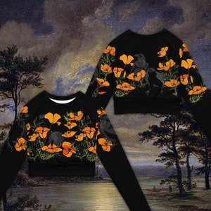 May include: Black long-sleeved crop top with a floral print of orange poppies and black birds. The top has a crew neck and a relaxed fit.