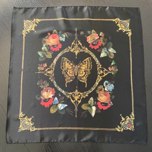 May include: Black silk scarf with a gold and floral design. The center of the scarf features a gold butterfly with a floral border.