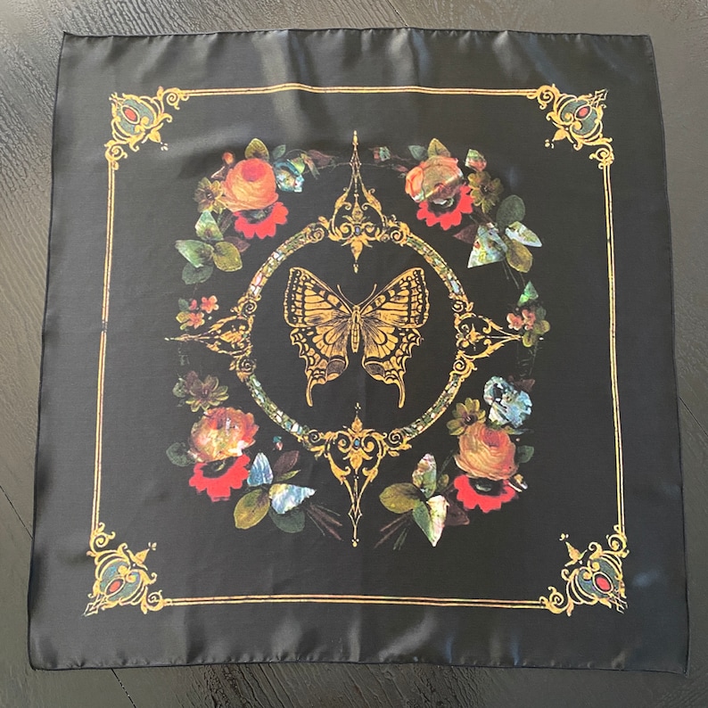 May include: Black silk scarf with a gold and floral design. The center of the scarf features a gold butterfly with a floral border.