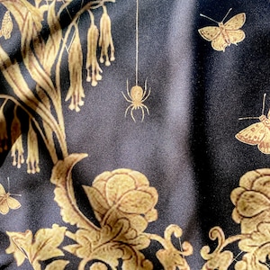 May include: Black fabric with a gold floral pattern, including butterflies and spiders. The fabric has a subtle sheen and a soft texture.