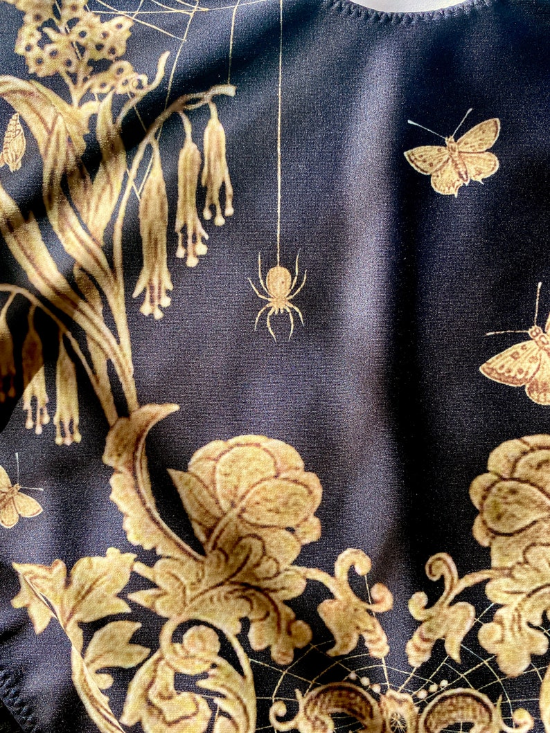 May include: Black fabric with a gold floral pattern, including butterflies and spiders. The fabric has a subtle sheen and a soft texture.