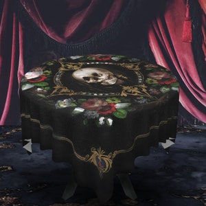 May include: Black round tablecloth with a skull and floral design. The skull is surrounded by a gold frame and red roses. The tablecloth has a scalloped edge.