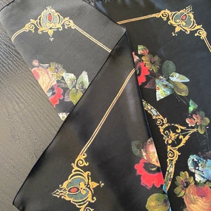 May include: Black silk scarf with a floral pattern and gold accents. The flowers are red, white, and blue. The scarf has a square shape and is folded in half.