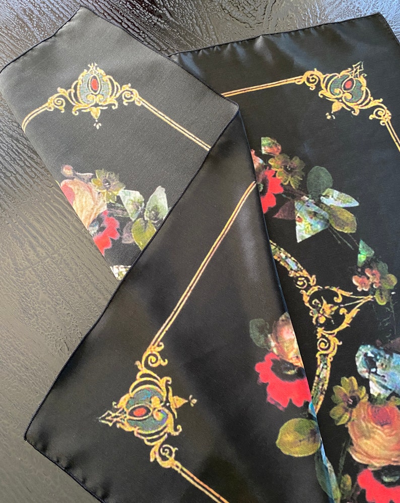 May include: Black silk scarf with a floral pattern and gold accents. The flowers are red, white, and blue. The scarf has a square shape and is folded in half.