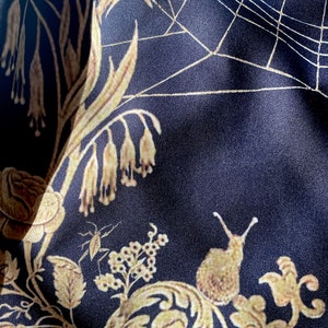 May include: Black fabric with a gold floral pattern, including a snail, a spider web, and a small insect. The fabric has a satin-like sheen.