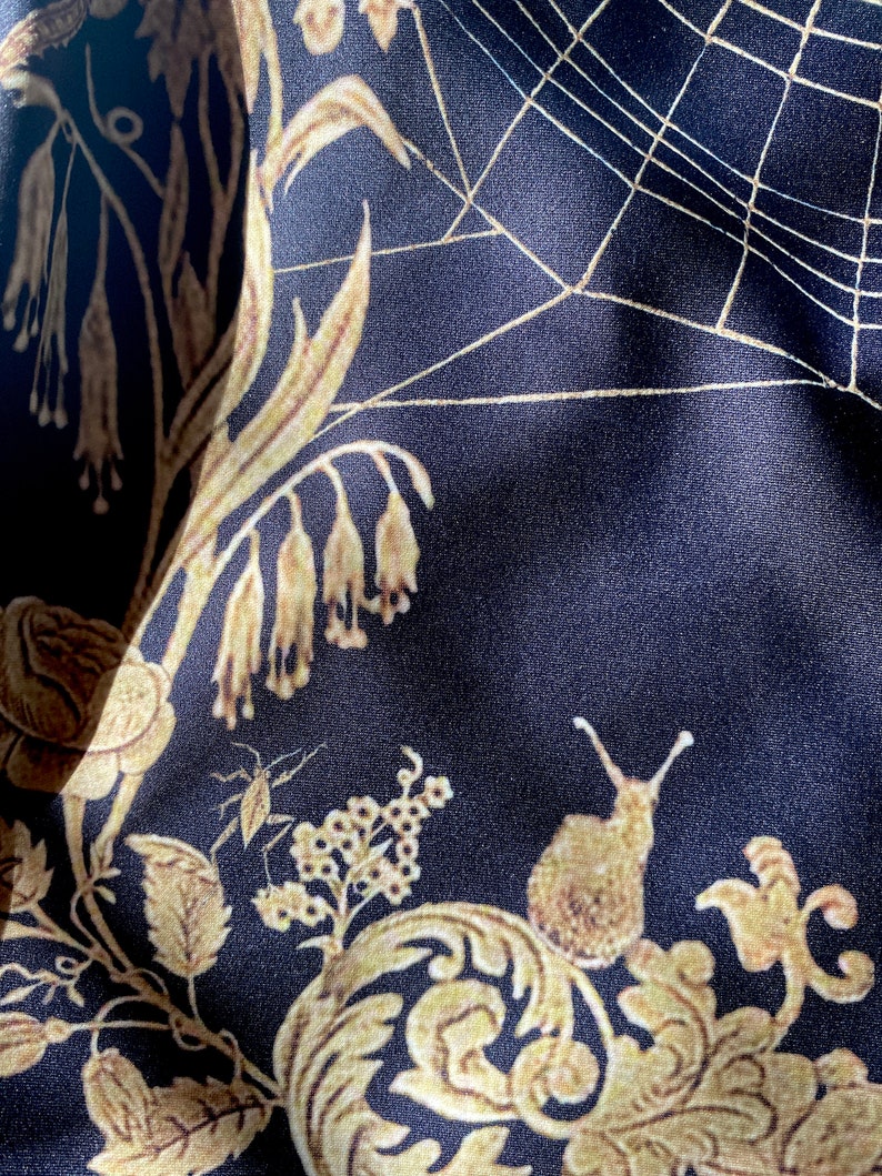 May include: Black fabric with a gold floral pattern, including a snail, a spider web, and a small insect. The fabric has a satin-like sheen.