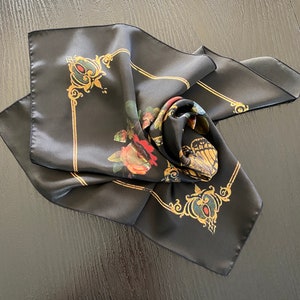 May include: Black silk scarf with a floral and butterfly design. The scarf features gold accents and a decorative border.