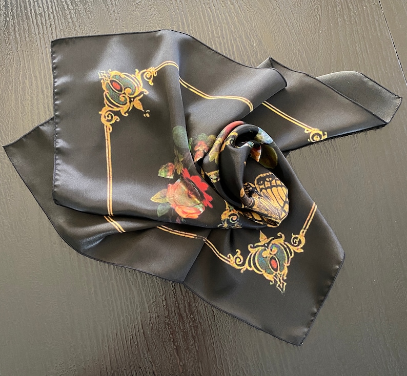 May include: Black silk scarf with a floral and butterfly design. The scarf features gold accents and a decorative border.