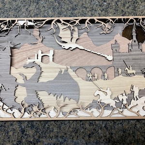 May include: A wooden wall art piece depicting a fantasy scene with dragons, knights, and a castle. The art is intricately cut and layered, creating a 3D effect.