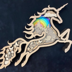 Puede incluir: Una escultura de unicornio de madera con un arcoíris, un castillo y nubes en su interior. El unicornio está saltando con su cuerno apuntando hacia adelante.