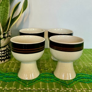 Może przedstawiać: Zestaw czterech białych ceramicznych misek z brązowymi i czarnymi paskami. Miski mają podstawę na nóżce.