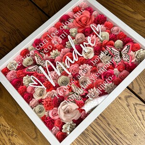 Pu&ograve; includere: Una cornice bianca piena di fiori di carta rosa, rossi e crema. I fiori sono disposti a forma di cuore con la parola "Madre" in lettere bianche al centro. Il testo "Te veo con los ojos que veo a mi Madre: amor, bondad, humildad y empatia. Te quiero." &egrave; scritto in lettere bianche intorno ai fiori.