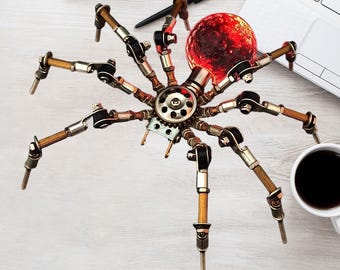 May include: A steampunk spider sculpture with a red, orb-shaped body. The spider's legs are made of metal and wood, with intricate mechanical details. A coffee cup, laptop, and notepad are in the background.