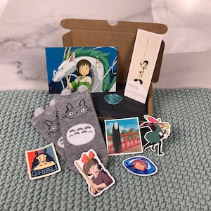 May include: A pair of grey and white socks featuring a Totoro character design. The socks are packaged in a cardboard box with various Studio Ghibli character illustrations and the text "Totoro".