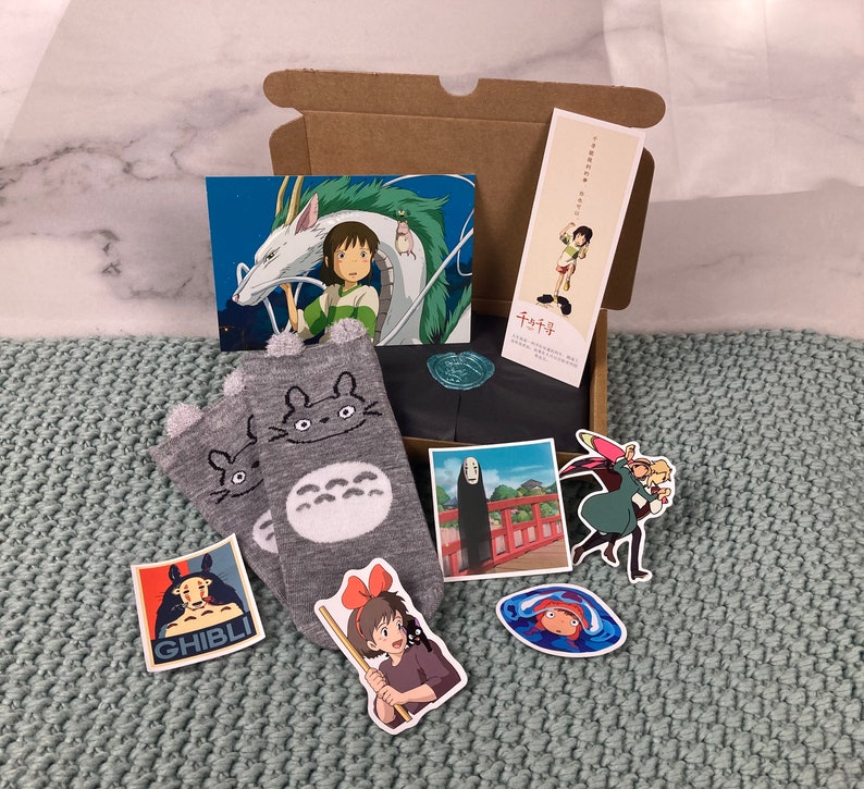 May include: A set of two grey and white socks with a Totoro character design. The socks are packaged in a cardboard box with various Studio Ghibli character illustrations and the text "Totoro".
