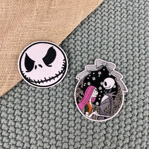 May include: Two embroidered iron-on patches featuring characters from The Nightmare Before Christmas. The first patch is a close-up of Jack Skellington's face. The second patch shows Jack Skellington and Sally standing together.