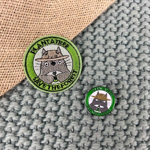 May include: Two embroidered iron-on patches featuring a cartoon cat wearing a ranger hat and holding a sapling. The patches are green and white with the text "Plant a Tree Save the Forest".