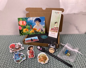 May include: A cardboard box filled with various items, including a bookmark with Japanese text, a postcard with a scene from the animated film "Spirited Away", and several stickers featuring characters from the film. The stickers include No Face, Totoro, and Chihiro.