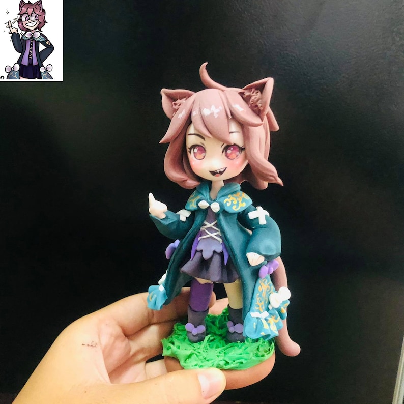 May include: A handmade figurine of a cartoon character with pink hair, cat ears, and a green and purple outfit. The figurine is standing on a green base.