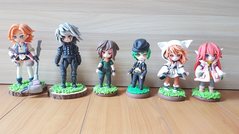 May include: Seven small, hand-painted figurines of anime characters. The figurines are made of clay and are painted in various colours, including black, white, green, pink, and orange. Each figurine is standing on a small, green base.
