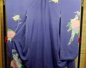 May include: A purple kimono with a floral pattern in shades of pink, white, and green. The kimono is hanging on a black stand.