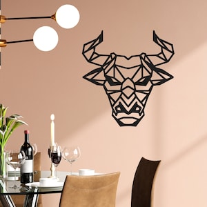 Op de afbeelding: Zwarte geometrische stierenkop wanddecoratie met een modern ontwerp. De stierenkop is gemaakt van metaal en heeft een zwarte afwerking. Het hangt aan een lichtroze muur in een eetkamer setting.