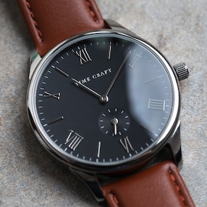 May include: A silver watch with a black face and Roman numeral hour markers. The watch has a brown leather strap and the words "Time Craft" are printed on the face.