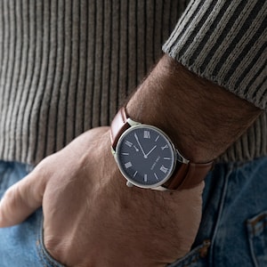 May include: A silver watch with a brown leather strap and a dark blue face. The watch has Roman numeral hour markers and a silver second hand.