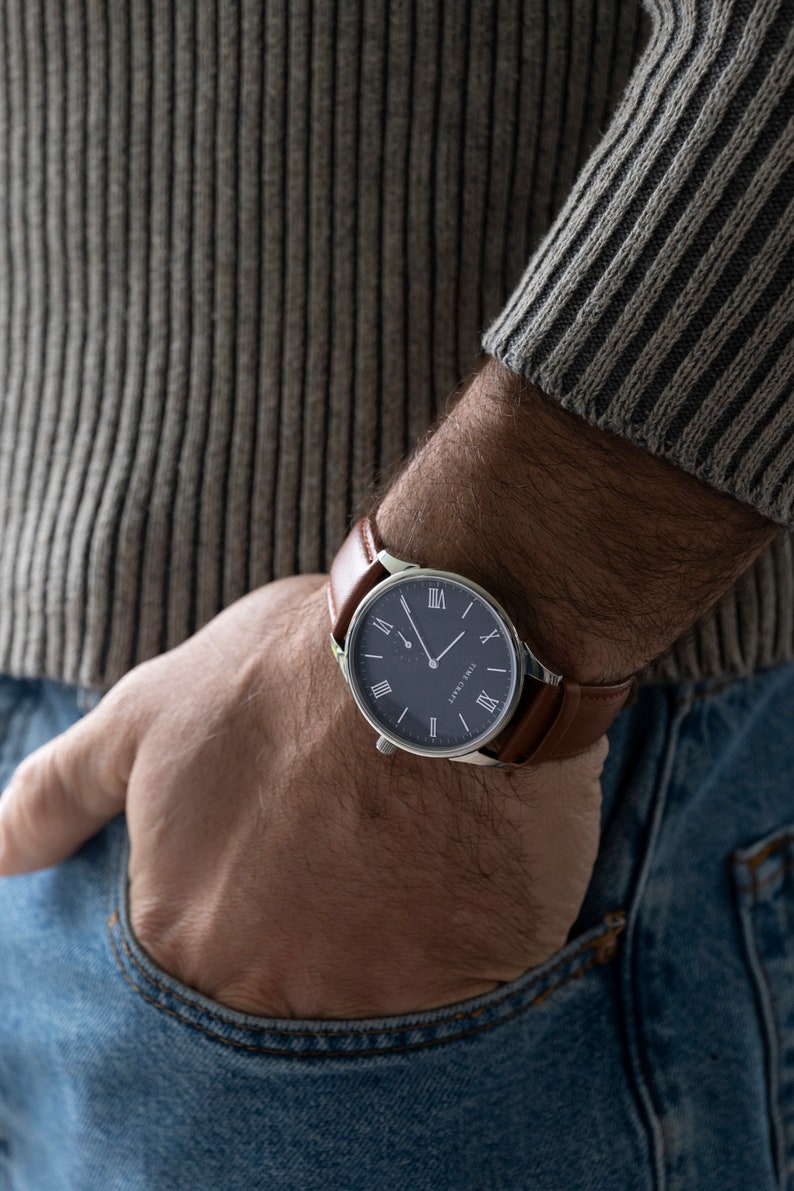 May include: A silver watch with a brown leather strap and a dark blue face. The watch has Roman numeral hour markers and a silver second hand.