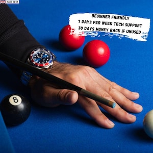 May include: A person's hand is positioned to strike a white cue ball with a pool cue on a blue felt table. The image includes red billiard balls, a black 8-ball, and a wristwatch. Text on the image reads: Beginner Friendly, 7 Days Per Week Tech Support, 30 Days Money Back If Unused.