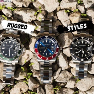 May include: Three stainless steel watches with black, green, and red bezels. The watch faces display the brand "TIME CRAFT". The watches are on a bed of rocks. The word "RUGGED" is written on a white banner above one watch, and the word "STYLES" is written on a black banner above another.