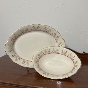 May include: Two oval-shaped ceramic serving dishes with a cream-coloured background and a gold rim. The dishes feature a green and red floral design with a gold ribbon.