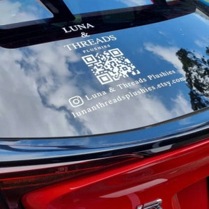 May include: A white sticker on the back window of a red car. The sticker says "Luna & Threads Plushies" and includes a QR code and the text "lunathreadsplushies.etsy.com".