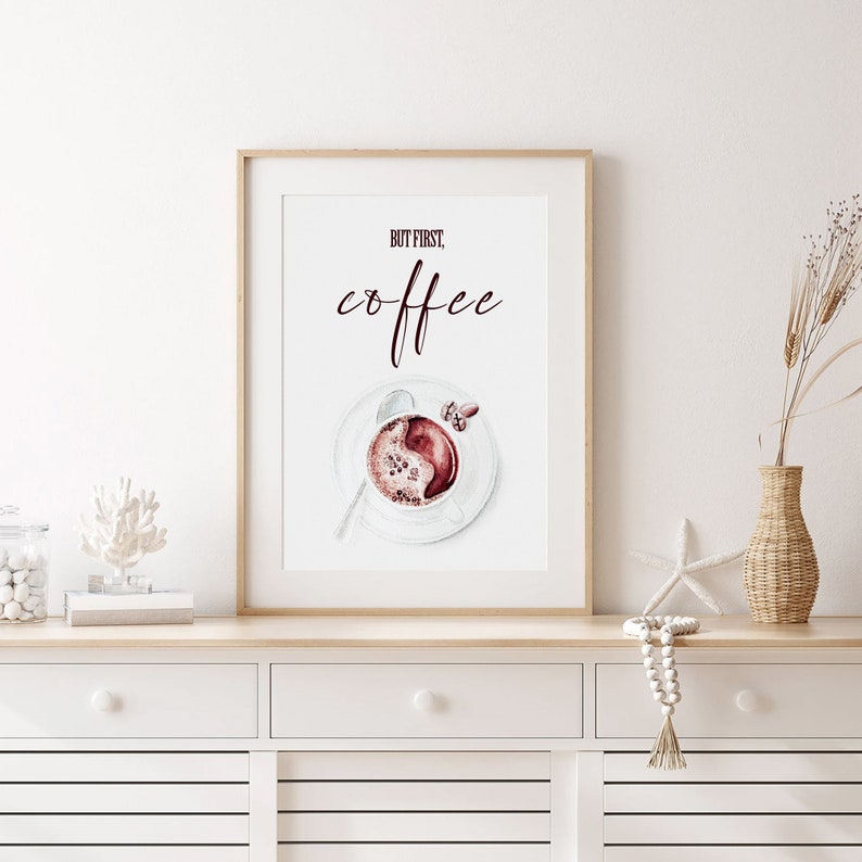 May include: A framed print with the text "But first, coffee" in a dark burgundy color. A watercolor illustration of a cup of coffee with a swirl of cream on top is below the text.