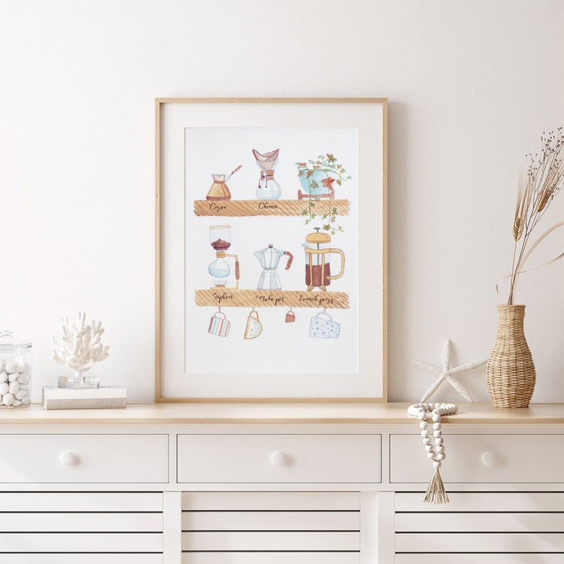 May include: A watercolor illustration of different coffee brewing methods, including a cezve, a Chemex, a syphon, a Moka pot, and a French press. The illustration is framed and displayed on a white shelf with a vase of dried flowers and a starfish.