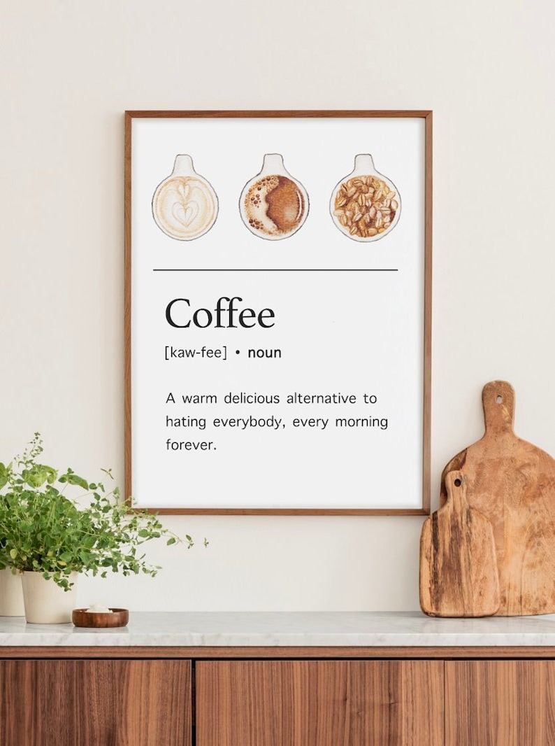 May include: A white framed print with a humorous definition of coffee. The print features three illustrations of coffee cups, one with latte art, one with black coffee, and one with coffee beans. The text reads "Coffee [kaw-fee] noun A warm delicious alternative to hating everybody, every morning forever."