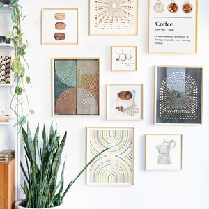 May include: A white wall with a collection of framed art prints. The prints feature geometric patterns, abstract designs, and illustrations of coffee beans and a coffee pot. A potted snake plant sits in front of the wall.