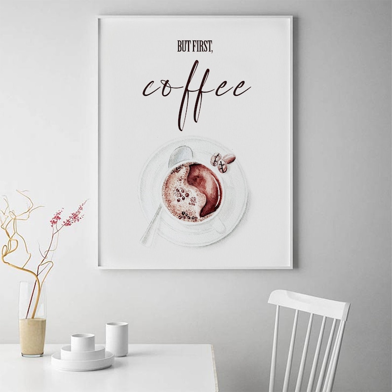 May include: A white poster with the text "But first, coffee" in maroon lettering. A watercolor illustration of a cup of coffee with coffee beans on a white saucer is below the text.
