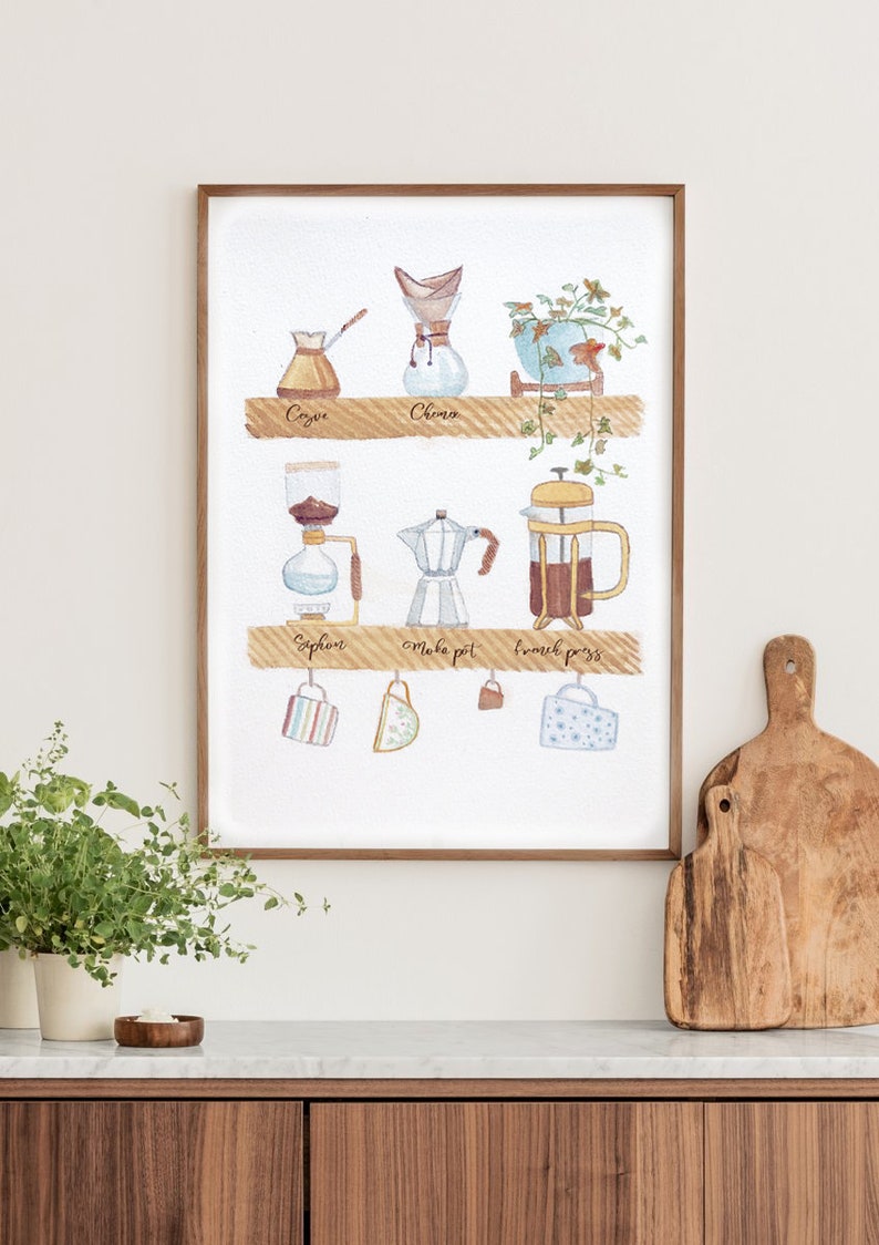 May include: A watercolor illustration of different coffee brewing methods, including a cezve, a Chemex, a siphon, a Moka pot, and a French press. The illustration is framed and hanging on a white wall above a wooden countertop.