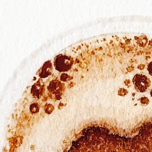 May include: Close-up of a watercolor painting of a coffee cup with brown and white paint. The coffee cup is filled with coffee and has a foam layer on top.
