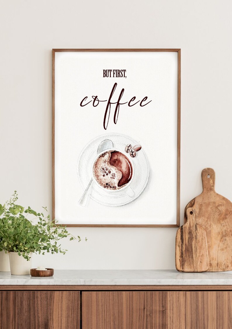 May include: A framed print with the text "But first, coffee" in brown lettering. A watercolor illustration of a cup of coffee with coffee beans on a white saucer is below the text.