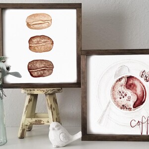 May include: Two framed watercolor paintings. The first painting features three coffee beans in a row. The second painting features a cup of coffee with the text "but first, coffee" in red.