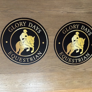 May include: Two circular black signs featuring a gold-colored graphic of a rider on a jumping horse. The text "GLORY DAYS" is arched across the top, and "EQUESTRIAN" is arched across the bottom in gold lettering, with small gold dots on the sides.