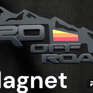 May include: Black metal magnet with a mountain range design and the words "TRD OFF ROAD" in raised lettering. The mountain range has a red, orange, and yellow stripe.
