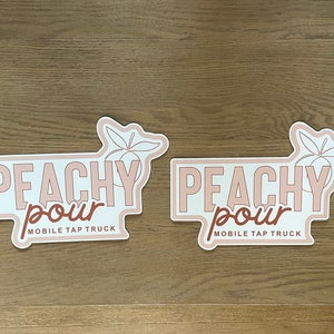 May include: Two identical die-cut stickers featuring the text PEACHY POUR MOBILE TAP TRUCK in a mix of block and script fonts. The design includes a line-art illustration of a peach with leaves, rendered in shades of light pink and brown.