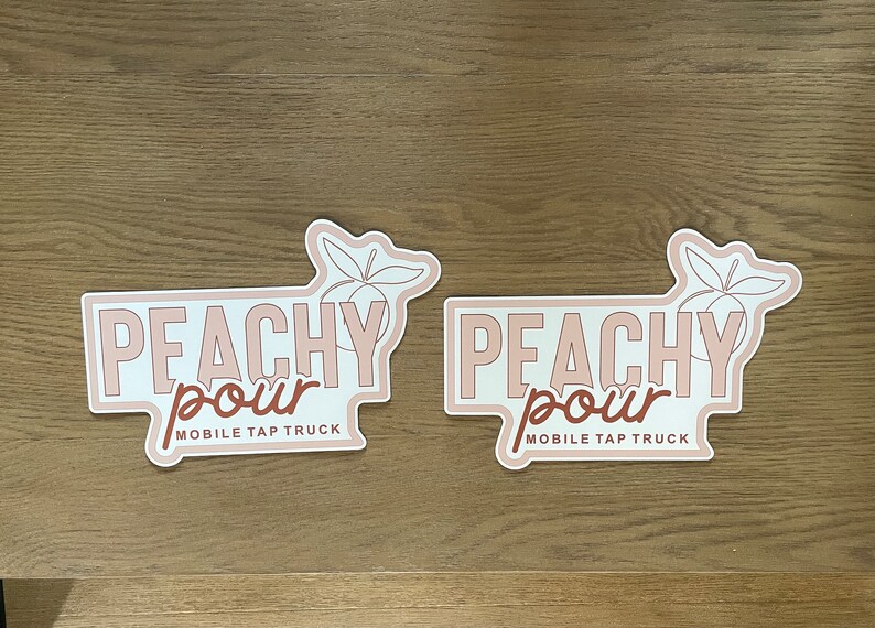 May include: Two identical die-cut stickers featuring the text PEACHY POUR MOBILE TAP TRUCK in a mix of block and script fonts. The design includes a line-art illustration of a peach with leaves, rendered in shades of light pink and brown.