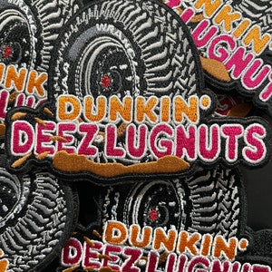 May include: A close-up of several embroidered patches featuring a tire with the text "Dunkin' Deez Lugnuts" in orange, pink, and white lettering on a brown background.