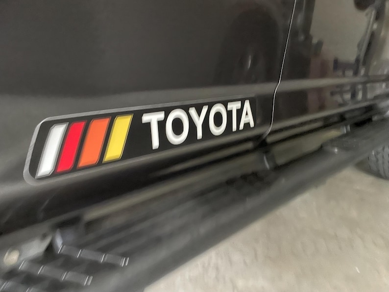 May include: A black Toyota truck with a red, orange, and yellow stripe and the word "TOYOTA" in white lettering on the side.