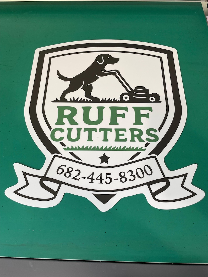 May include: A shield-shaped decal featuring a black silhouette of a dog pushing a lawnmower above the green text RUFF CUTTERS. Below the text is a white banner containing the black phone number 682-445-8300 and a small black star.